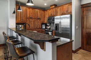 A kitchen with wooden cabinets, a stainless steel refrigerator, a microwave, a coffee maker, and a granite countertop. - Cozy Riverstone Escape | Walkable CDA Location (Coeur d'Alene)