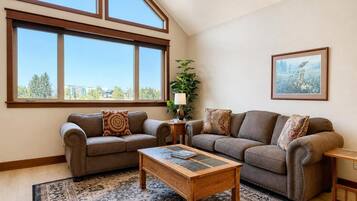 A living room with a high ceiling, large windows, a sofa set, a coffee table, and a patterned rug.