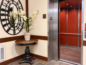 A lobby with a round table, a potted orchid, a wall-mounted mirror, and an elevator. - Unwind at Riverstone Loft (Coeur d'Alene)