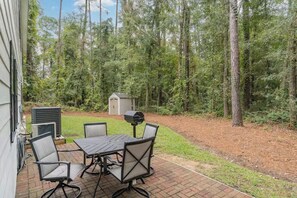 An outdoor patio with a table and chairs, surrounded by a wooded area. - Beach Retreat Near Pawleys Island w/ Open Living, Deck & Resort Amenities (Pawleys Island)