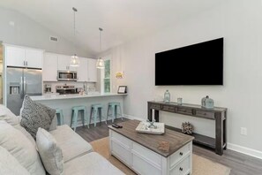 A modern kitchen with a central island, bar stools, and a large flat-screen TV mounted on the wall. - Beach Retreat Near Pawleys Island w/ Open Living, Deck & Resort Amenities (Pawleys Island)