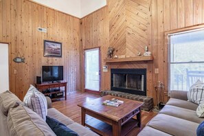 Una sala de estar con paredes de madera, chimenea, televisor y sofá.