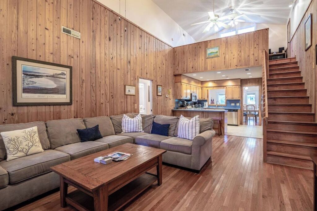 Una sala de estar con acabados de madera, un sofá seccional, una mesa de centro y una escalera que sube a un nivel superior.