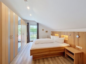 A modern bedroom with a large bed, wooden wardrobe, and a view of greenery outside. - Ferienhaus Siegele by Interhome (See)