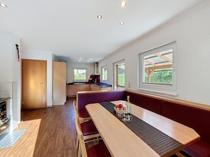A modern kitchen with wooden cabinets, a dining area with a bench, and a view of the outdoors through large windows. - Ferienhaus Siegele by Interhome (See)