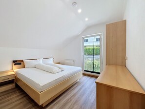 Ein Schlafzimmer mit einem Bett, einem Nachttisch, einem Holztisch und einem großen Fenster mit Blick auf Grünflächen.