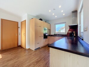 A modern kitchen with wooden cabinets, a built-in oven, and a large window with a mountain view. - Ferienhaus Siegele by Interhome (See)