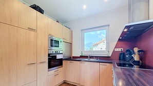 Eine moderne Küche mit Holzausstattung, einem Einbauofen, einer Mikrowelle und einem Fenster mit Blick auf die Berge.