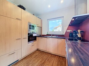 Eine moderne Küche mit Holzausstattung, einem Einbauofen, einer Mikrowelle und einem Fenster mit Blick auf die Berge.