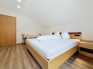 A bedroom with a wooden bed, a nightstand, a chair, and a door. - Ferienhaus Siegele by Interhome (See)