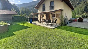 Ein zweistöckiges Haus mit einer Terrasse, einer Holzterrasse und Blick auf eine gebirgige Landschaft.