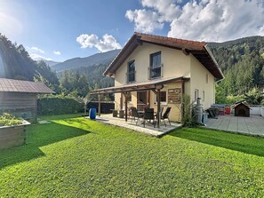 Ein zweistöckiges Haus mit einer Terrasse, einer Holzterrasse und Blick auf eine gebirgige Landschaft.