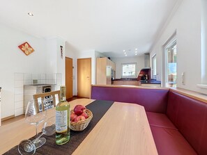A modern kitchen with a dining area featuring a wooden table, a red cushioned bench, and a basket of apples. - Ferienhaus Siegele by Interhome (See)
