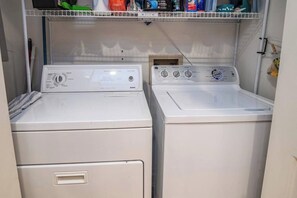 A laundry area with two stacked washing machines and a shelf above containing various cleaning supplies. - Beach House Near North Litchfield w/ Spacious Living Areas & Outdoor Deck (Pawleys Island)