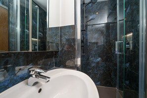 A modern bathroom with a white sink, a glass shower enclosure, and dark marble walls. - Holland Park W11 3 bed flat near tube and Westfield Mall (London)