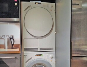 Eine kompakte, moderne Küche mit integrierter Waschmaschine und Trockner, Edelstahlgeräten und einem Wasserkocher auf der Arbeitsfläche.