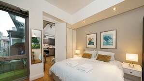Moderni hotellihuone, jossa on suuri sänky, yöpöytävalaisimet, näkymä lasiovesta ja taideteoksia seinillä.