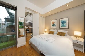 Ein modernes Hotelzimmer mit einem großen Bett, Nachttischlampen, Blick durch eine Glastür und Kunstwerken an den Wänden.