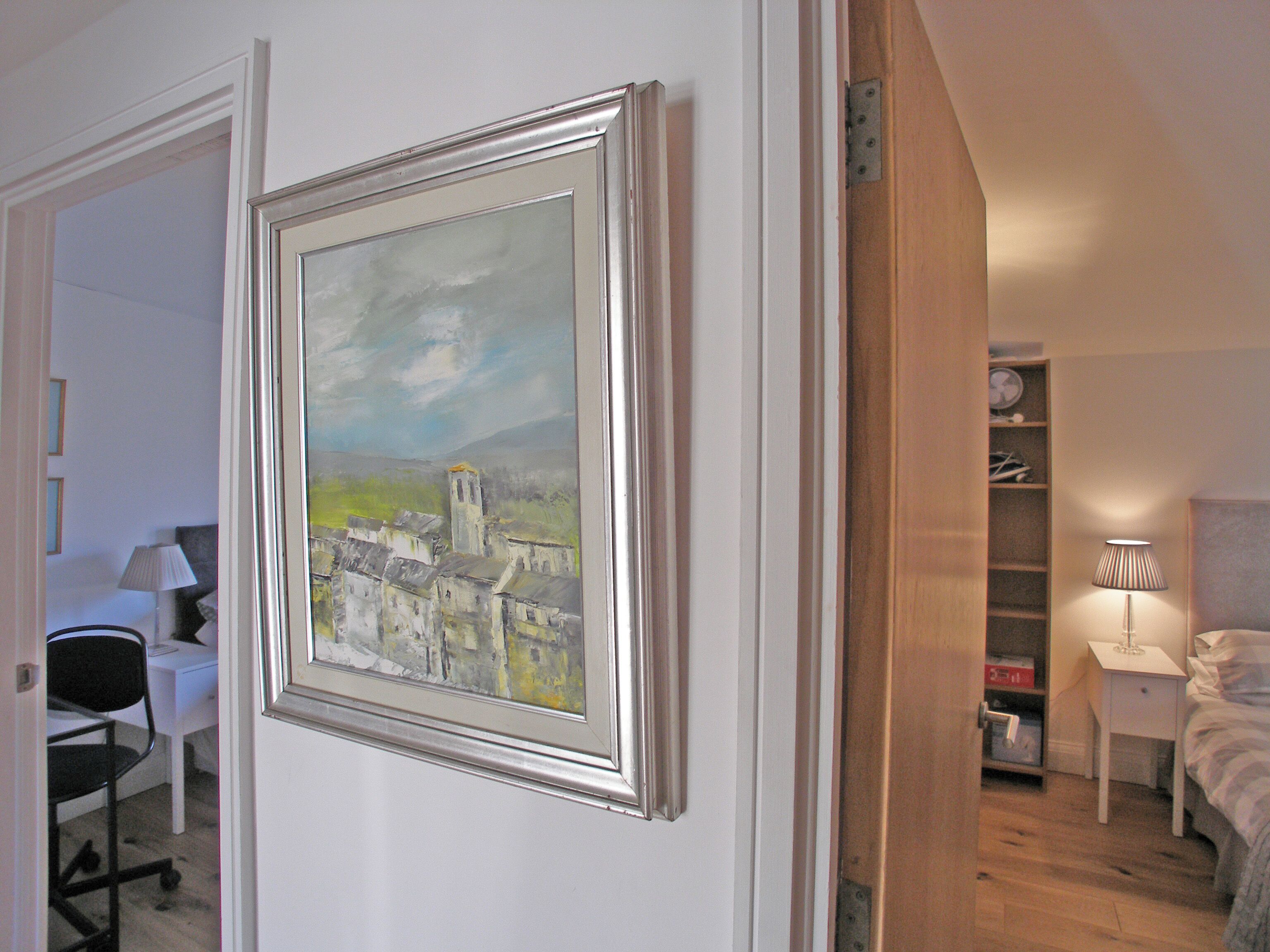 A bedroom with a bed, bedside table, lamp, and a framed painting on the wall.