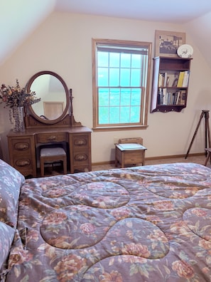 Ein Schlafzimmer mit Bett, Kommode, Spiegel, Fenster und Bücherregal.