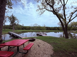 Ein Picknickplatz mit Tisch und Bänken, ein Steg und ein ruhiger See, umgeben von Bäumen.