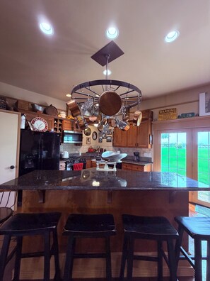 Una cocina con una isla central, ollas colgantes y un letrero de advertencia en la pared.
