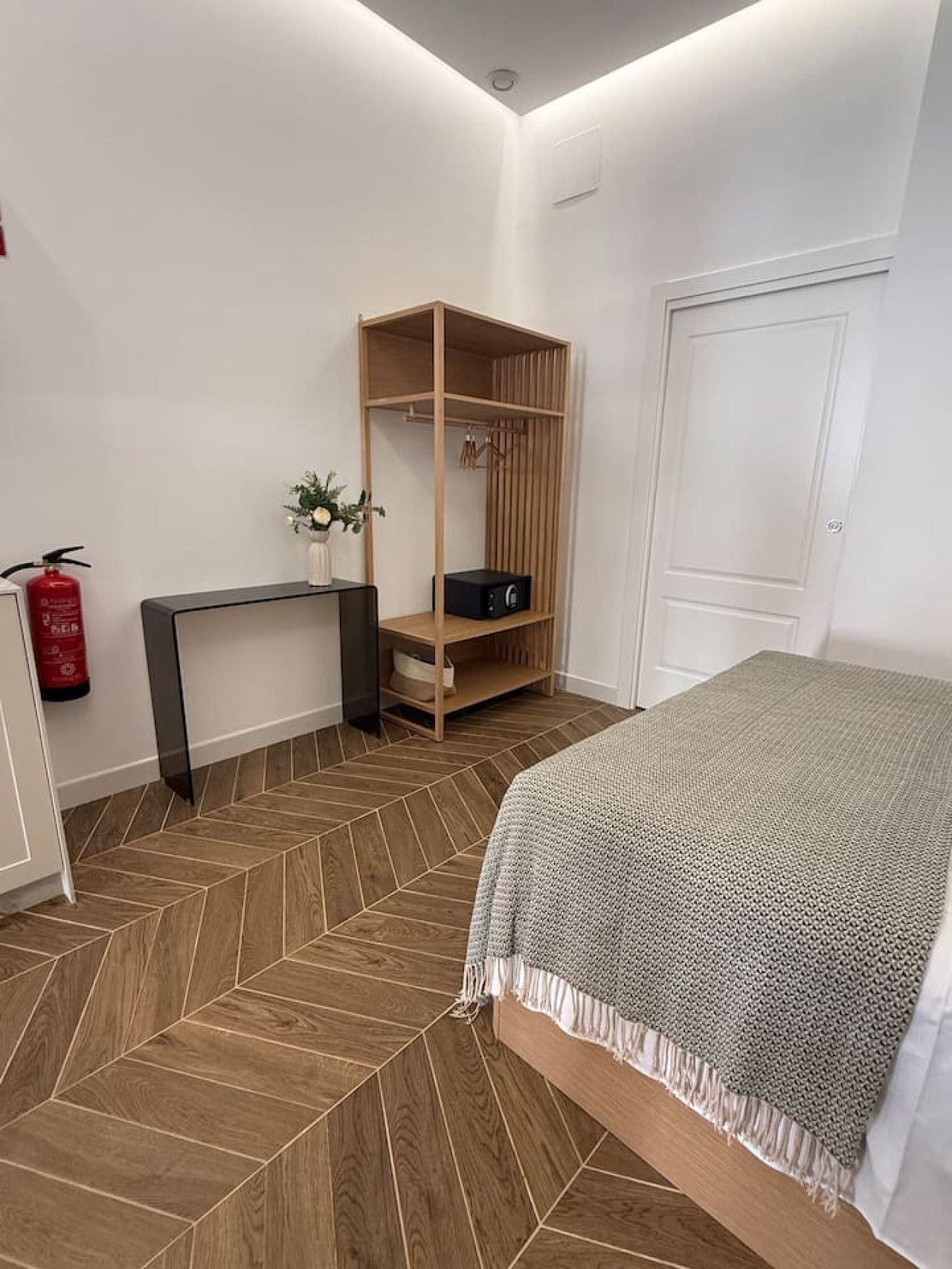 Une chambre à coucher avec un lit, une armoire en bois, une petite table avec un vase et un extincteur.