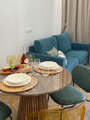 Ein Esstisch ist mit Tellern, Gläsern und einer Weinflasche gedeckt, im Hintergrund ein blaues Sofa.