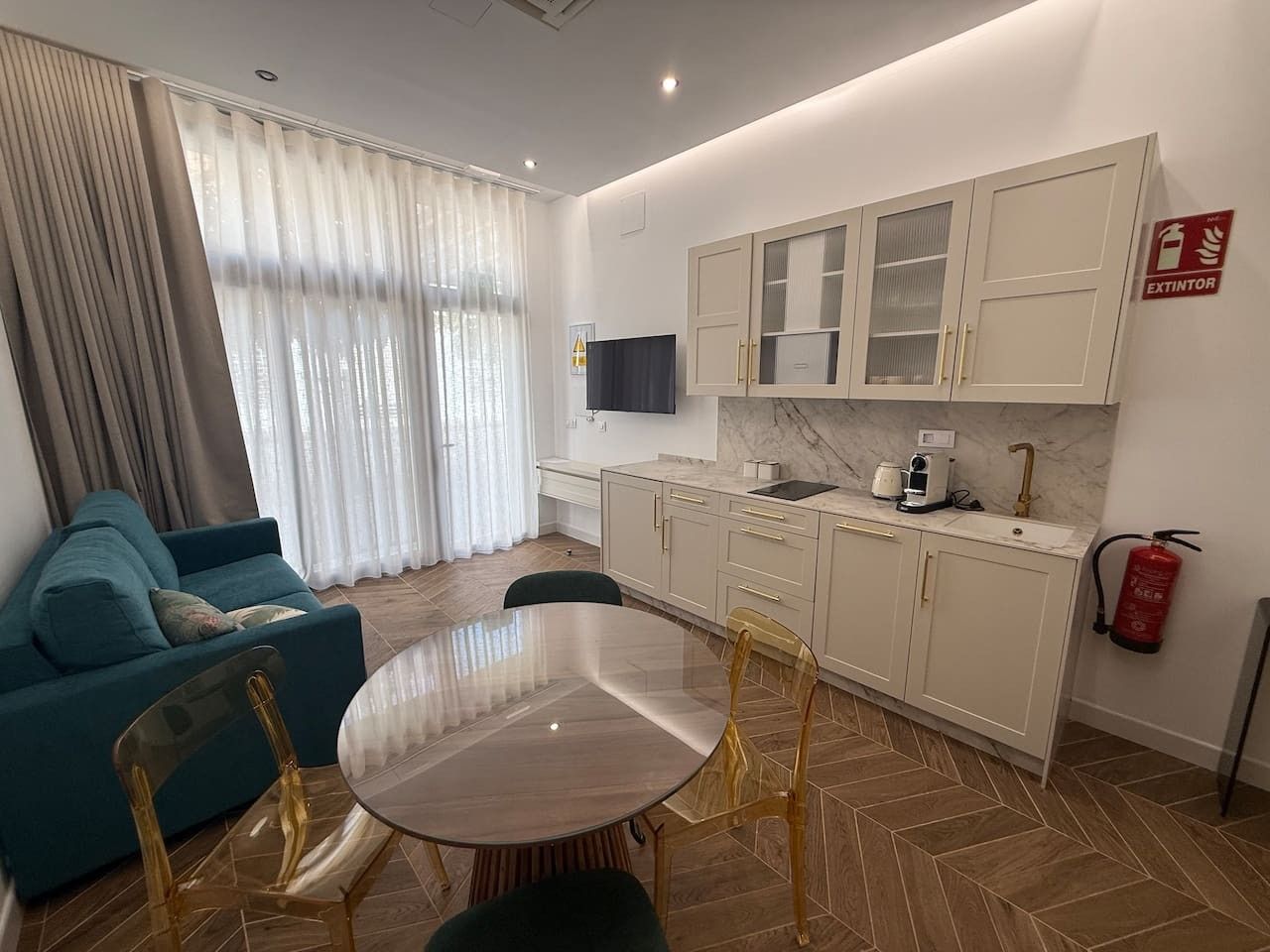 Un salon moderne comprenant un canapé, une table à manger et des chaises. On y trouve également un coin cuisine avec des placards et un extincteur.