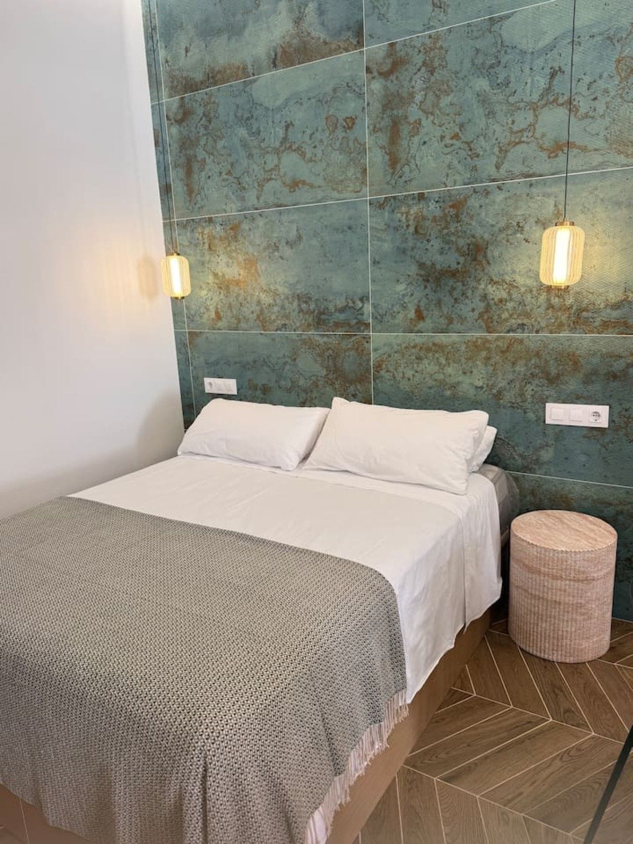 A bed with white linens, a textured throw blanket, and a woven side table.
