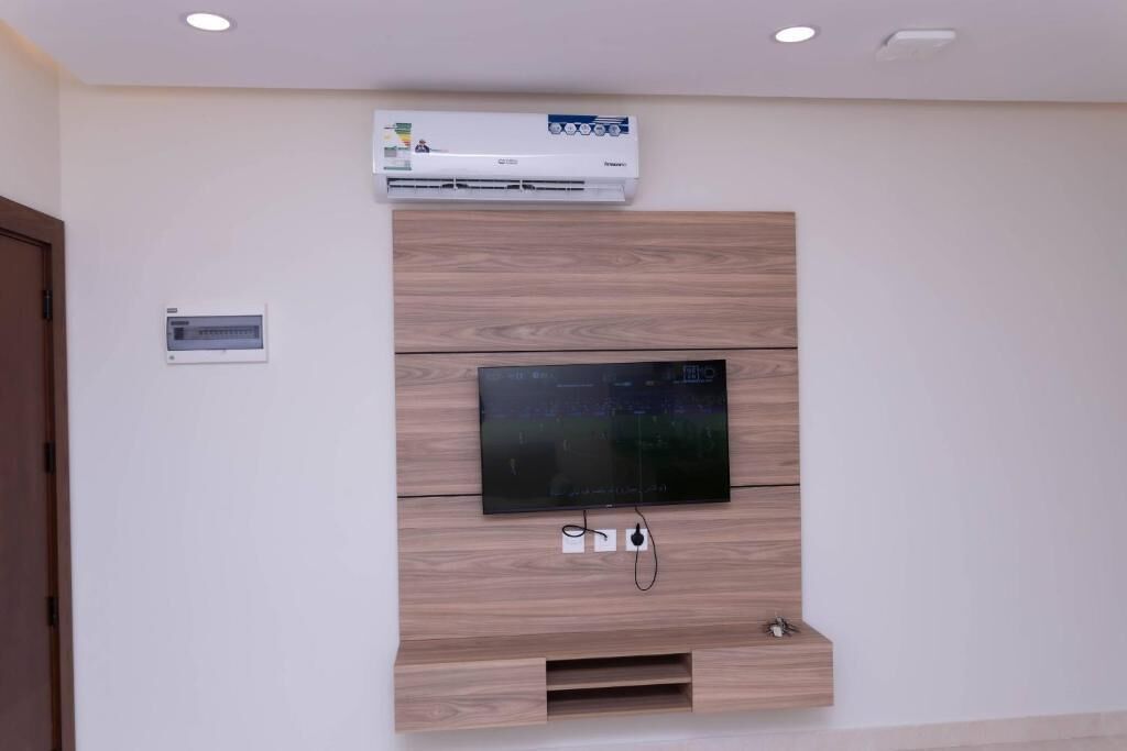 Ein modernes Wohnzimmer mit integriertem Fernseher, Holzvertäfelung und einer an der Wand montierten Klimaanlage.