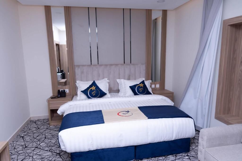A hotel room with a bed, a nightstand, a mirror, and a curtain.