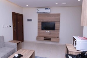 Uma sala de estar moderna com televisão de tela plana fixada em uma parede de madeira, um sofá cinza, uma mesa de centro de madeira e um micro-ondas em um armário de madeira.