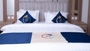 Habitación de hotel con una cama grande, dos almohadas con un logotipo, cabecero y mesita de noche.