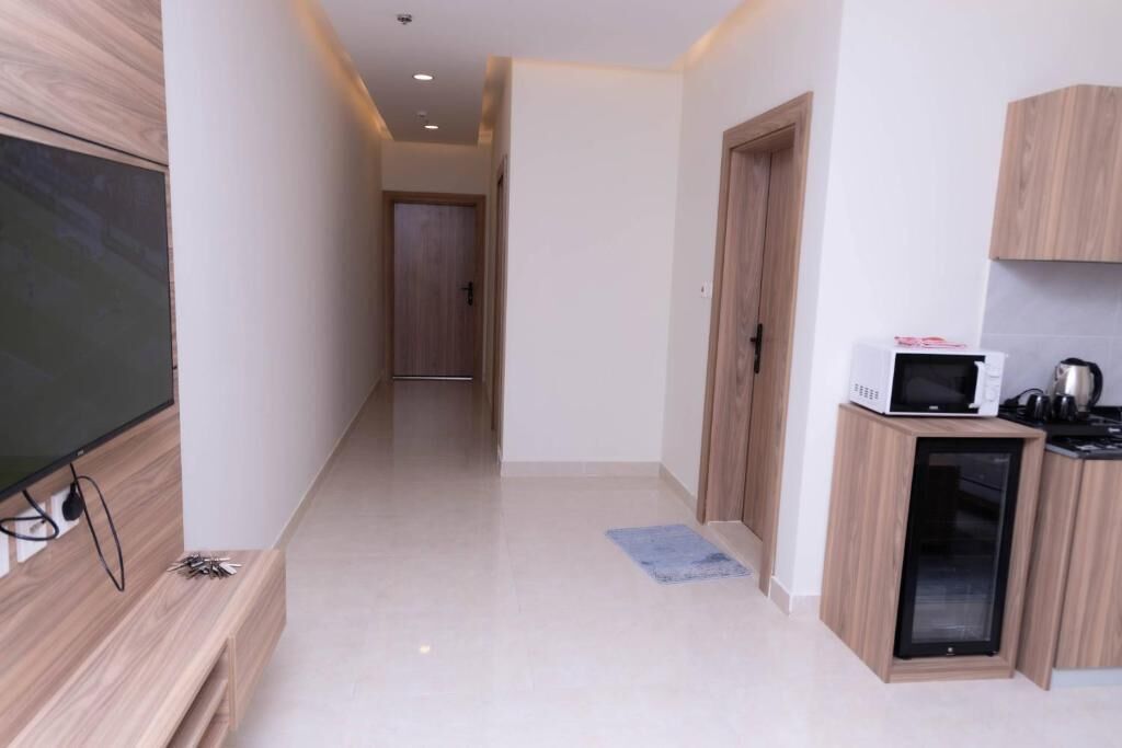 A hallway with a flat-screen TV on the left, a microwave and coffee maker on the right, and a door at the end.