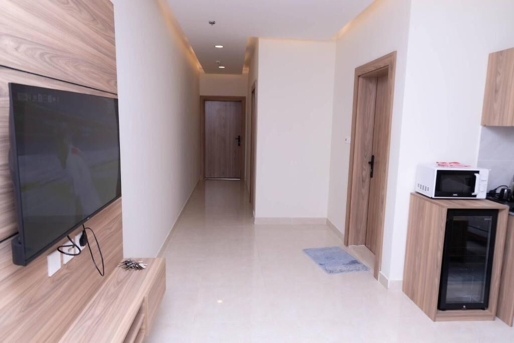 A hallway with a flat-screen TV mounted on the wall, a microwave on a cabinet, and a door leading to another room.