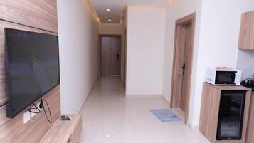 A hallway with a flat-screen TV mounted on the wall, a microwave on a cabinet, and a door leading to another room.
