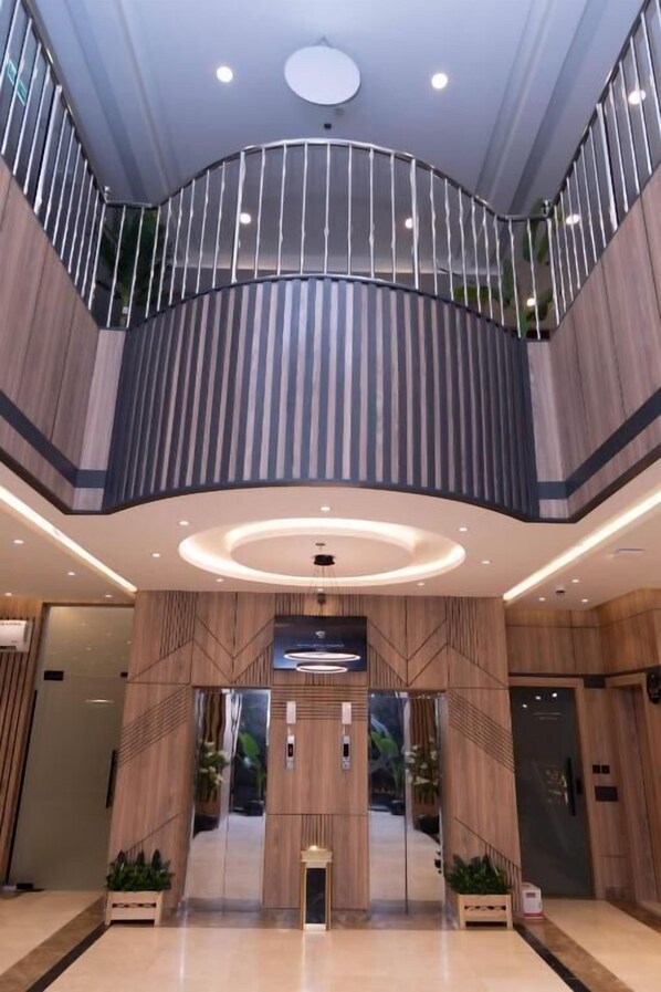 Um saguão de hotel moderno com elevador central, corrimão curvo e teto com iluminação embutida.