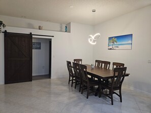 A dining area with a wooden table and chairs, a ceiling light, a door, and a wall-mounted picture.