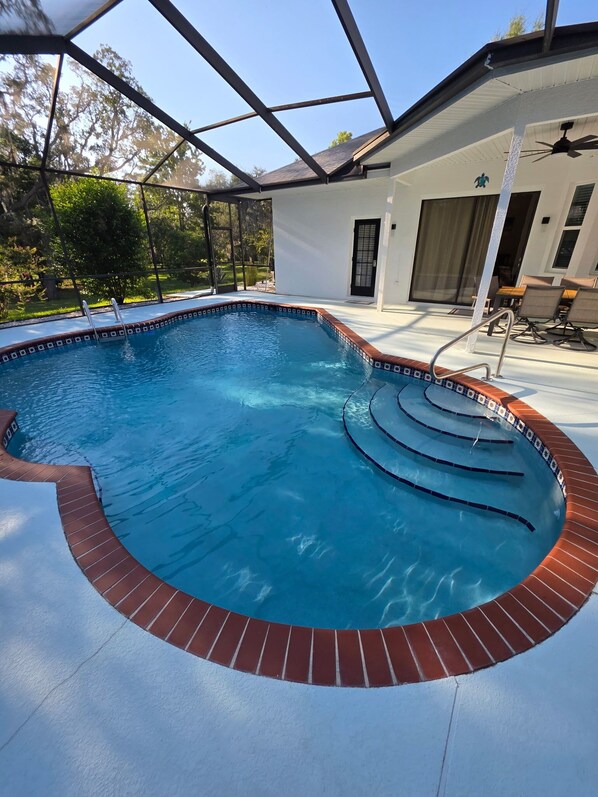 Piscina com borda de tijolos, área coberta com cadeiras e porta para um alpendre.
