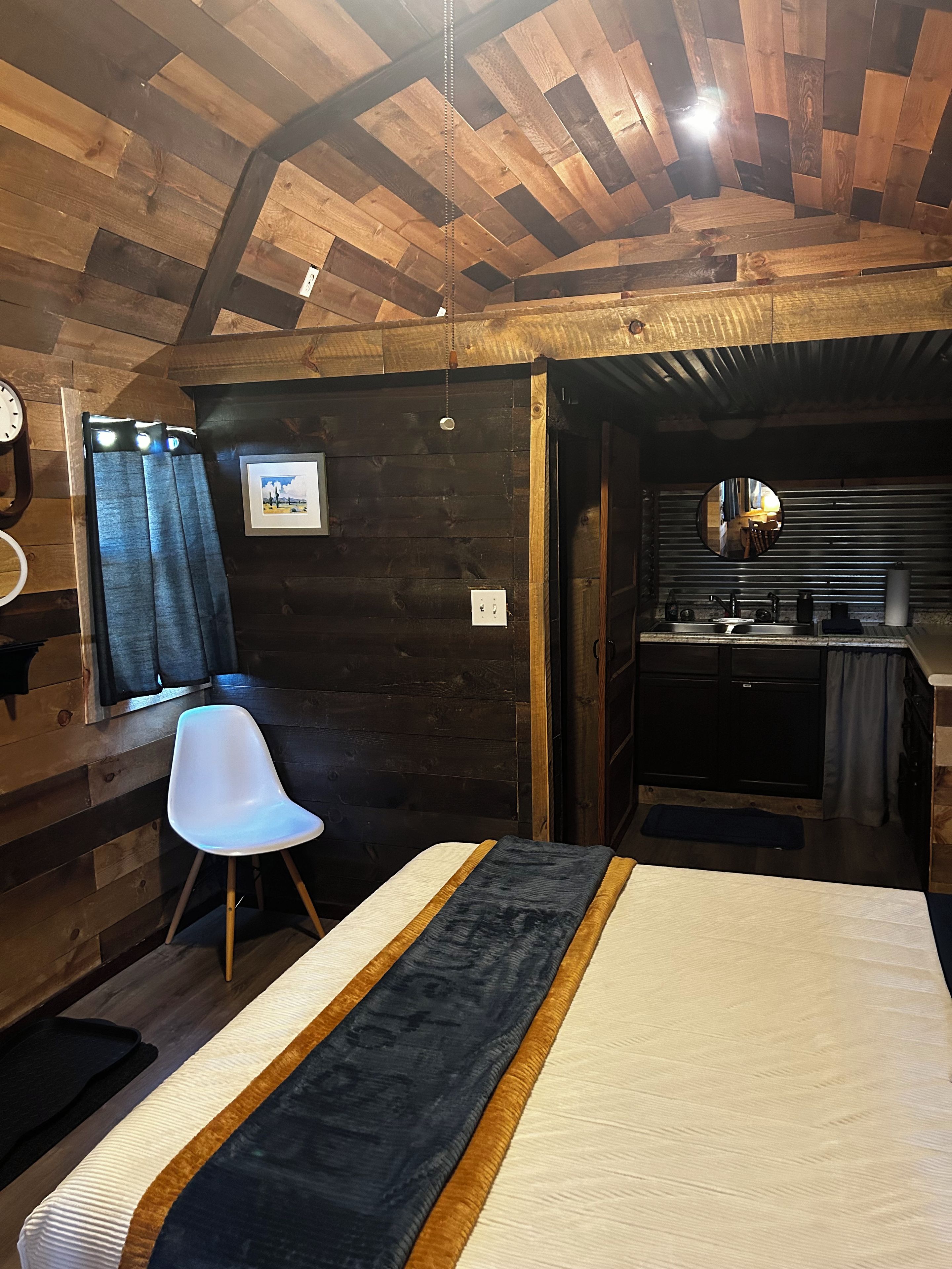 A room with a bed, a chair, a desk with a mirror, and a window with curtains.
