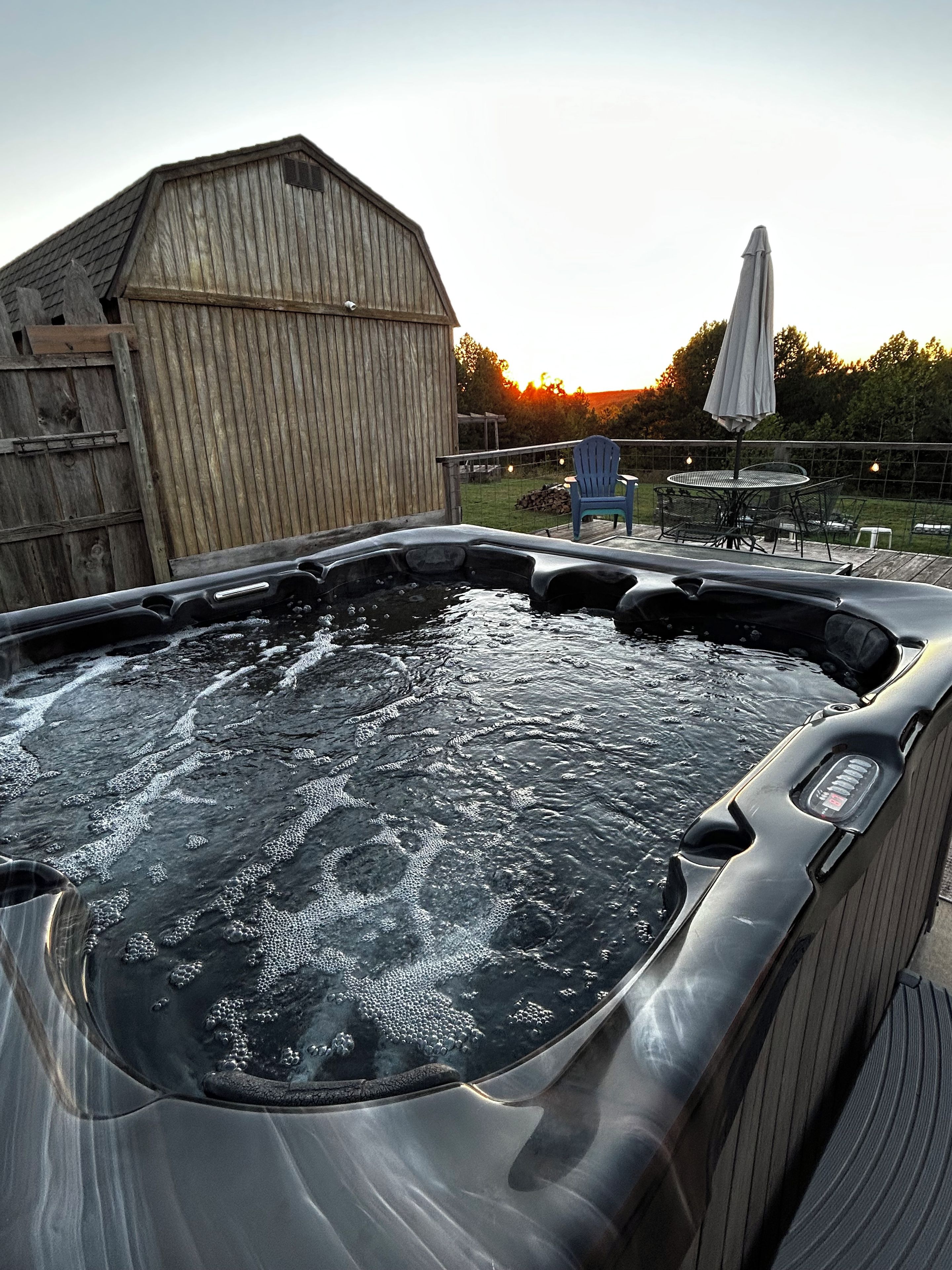 A hot tub with a wooden deck, a wooden shed, and a patio with outdoor furniture.