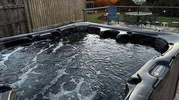 A hot tub with a wooden deck, a wooden shed, and a patio with outdoor furniture.