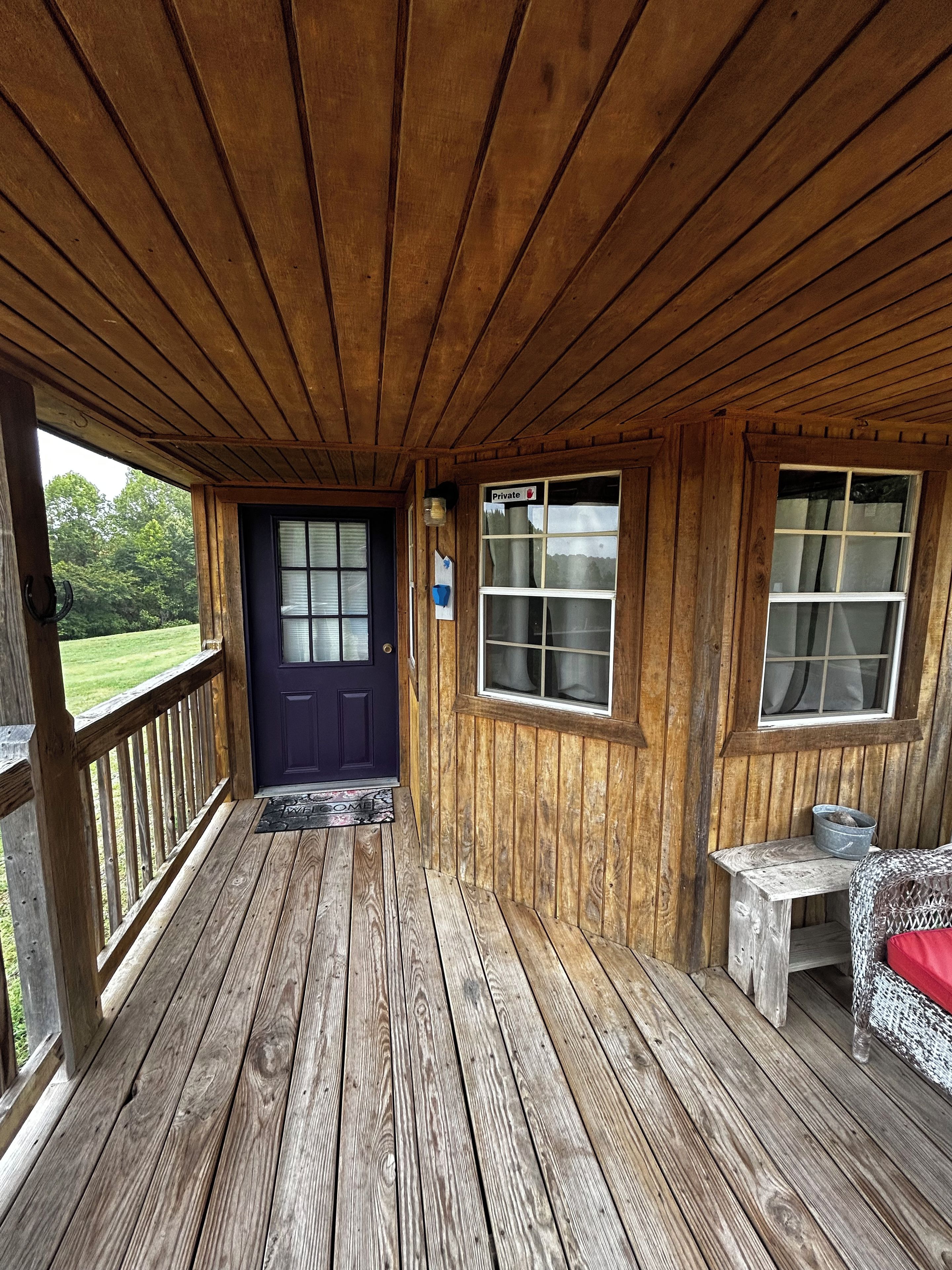 A wooden porch with a dark door, a small table with a red cushion, and a window with a sign indicating 'Private.'