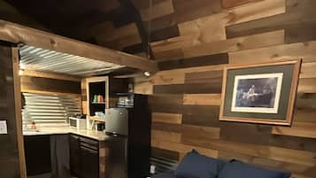 Un dormitorio con cama, mesita de noche, un cuadro enmarcado en la pared y una zona de kitchenette.
