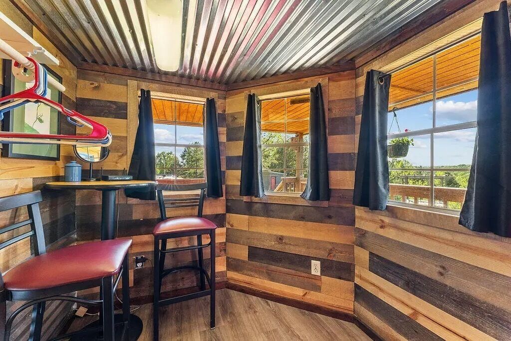 A room with wooden panel walls, a table with chairs, and large windows with curtains.