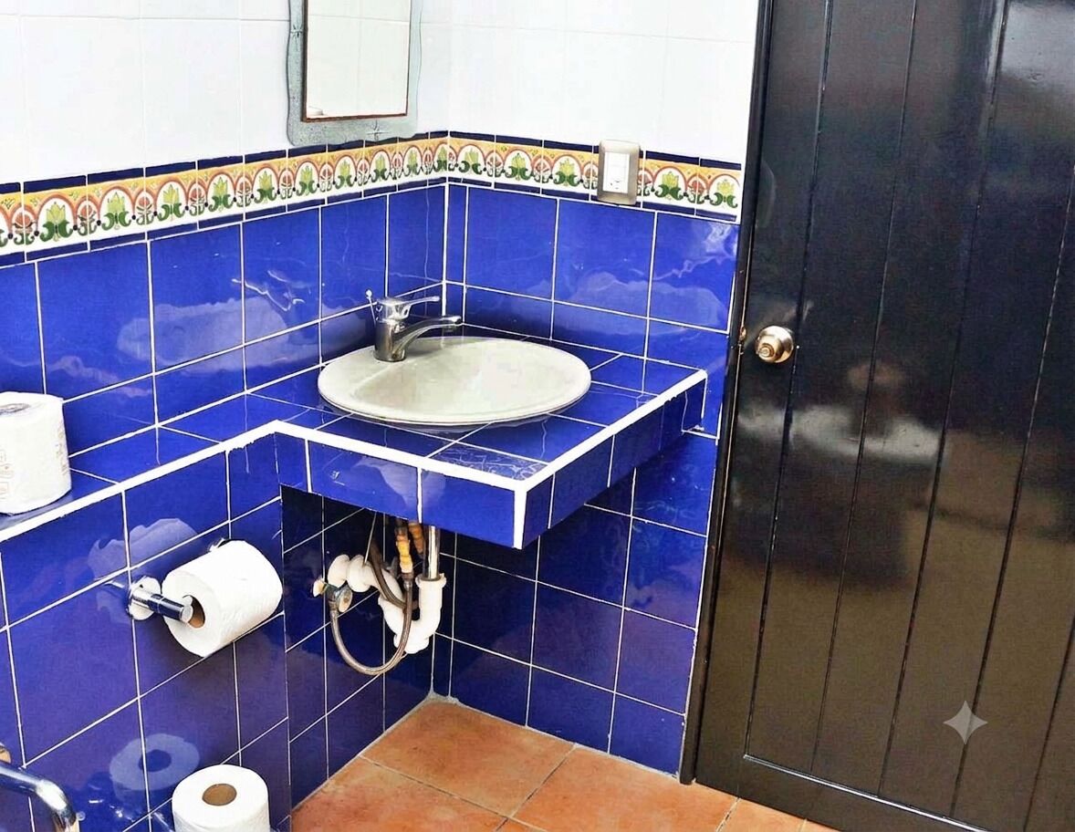 Un baño con azulejos azules, un lavamanos, un dispensador de papel higiénico y una puerta.
