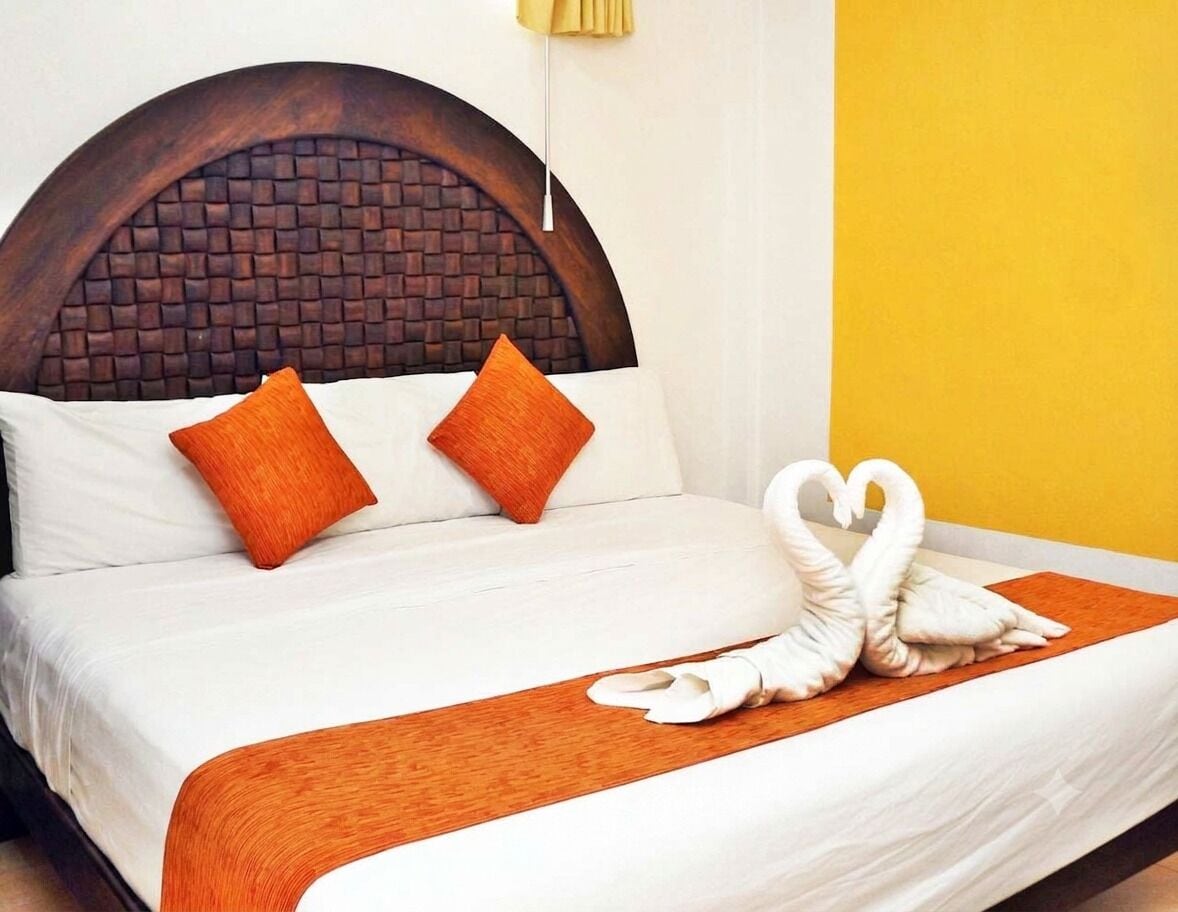 A hotel room with a bed, two pillows, a wooden headboard, and a swan-shaped pillow.