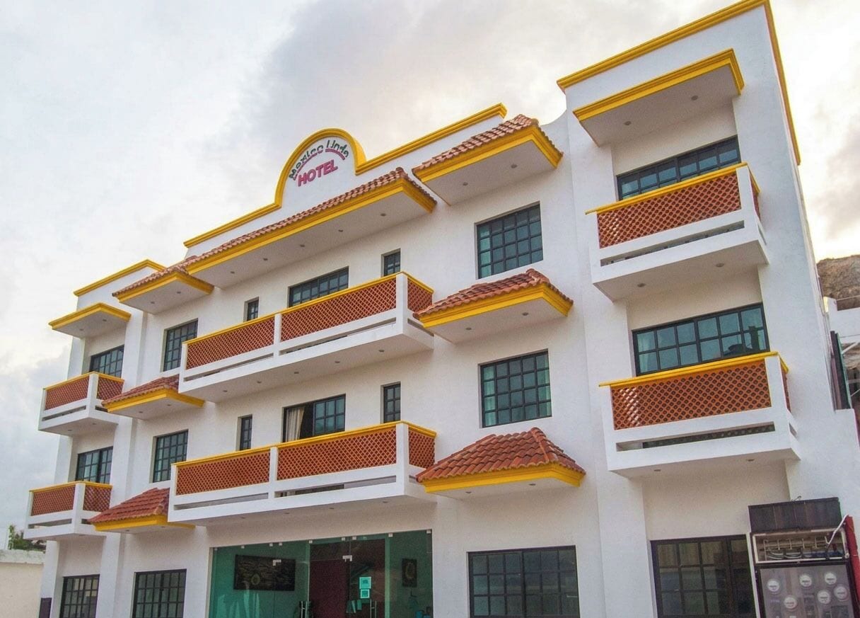 Un hotel de varios pisos con balcones, un letrero que indica que es un hotel y una entrada verde.