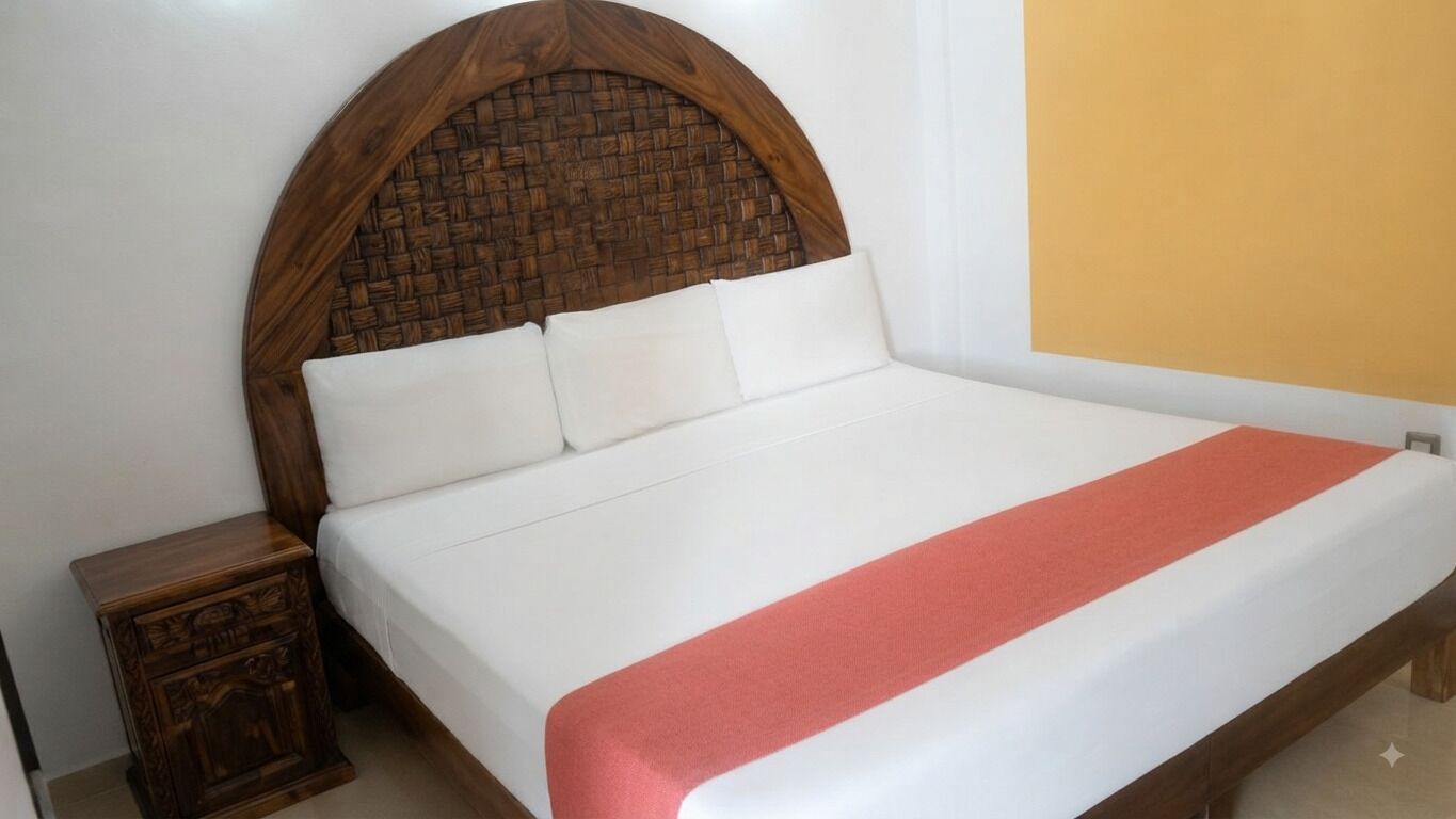 A bed with a wooden headboard, white bedding, and a red accent.